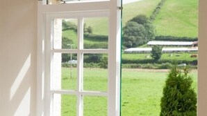 A window with a view of a green landscape, including a hill and a building in the distance. - Anchor Inn (Dulverton)