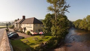 A riverside hotel with a grassy lawn, picnic tables, and umbrellas. - Anchor Inn (Dulverton)