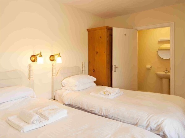 A hotel room with two beds, a wooden wardrobe, a bathroom with a sink and toilet, and wall-mounted lighting.