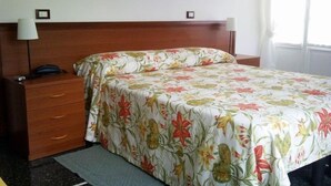 Quarto de hotel com cabeceira de madeira, colcha floral, mesa de cabeceira com abajur e telefone.