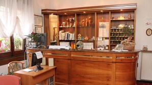Uma mesa de recepção com um computador, um telefone e uma planta. Há prateleiras com troféus e livros.