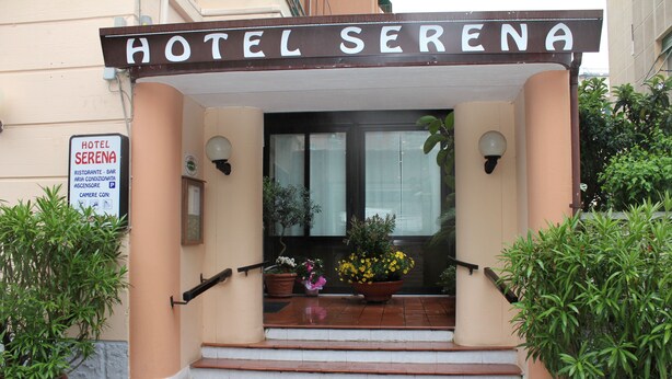 Entrada do Hotel Serena, com placa, degraus e plantas em vasos.