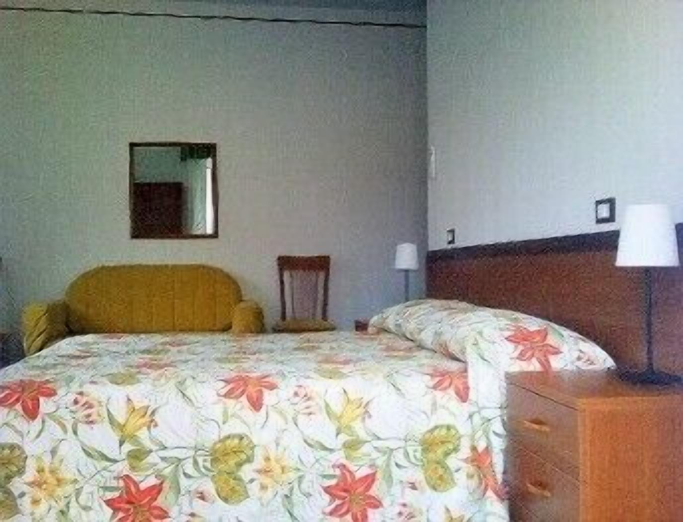 Een hotelkamer met een bed, een stoel, een nachtkastje en een lamp.