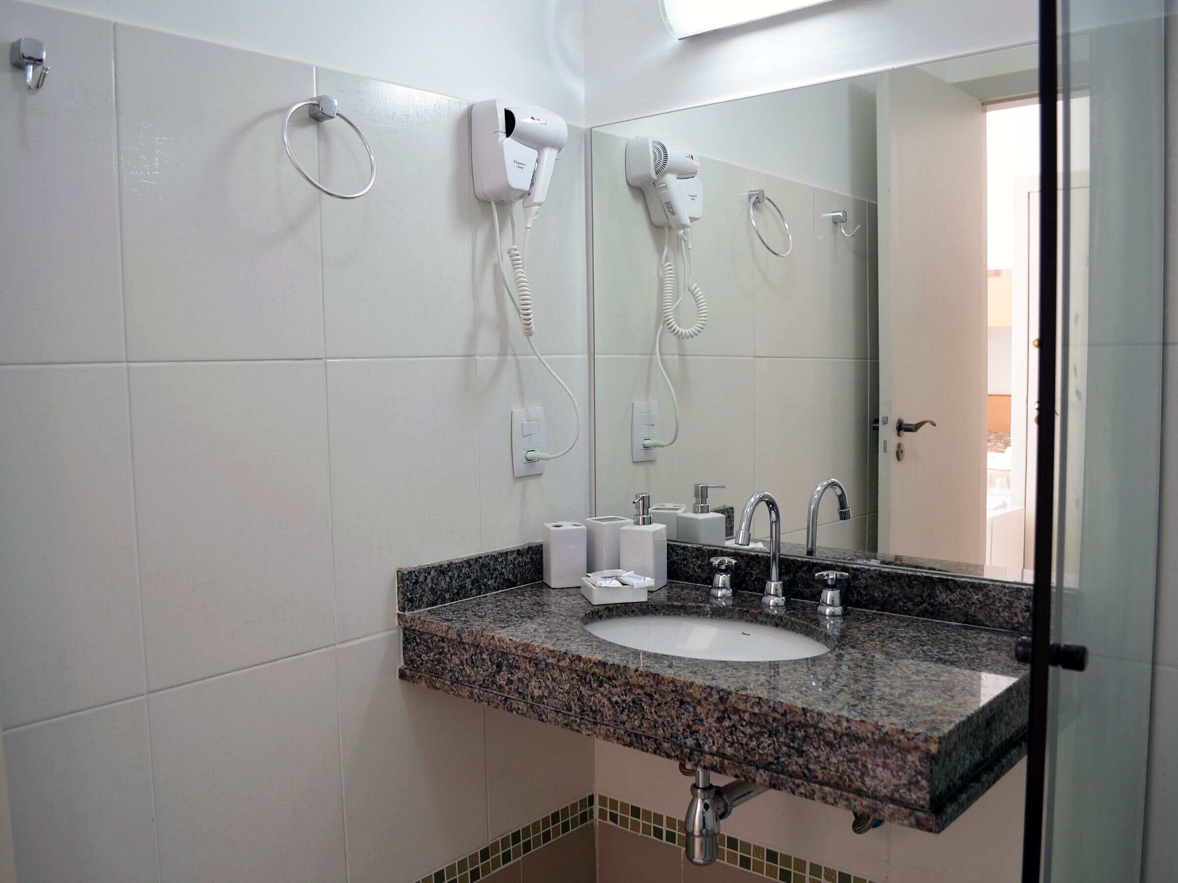 A bathroom with a granite countertop sink, a mirror, a hairdryer, and a towel ring.