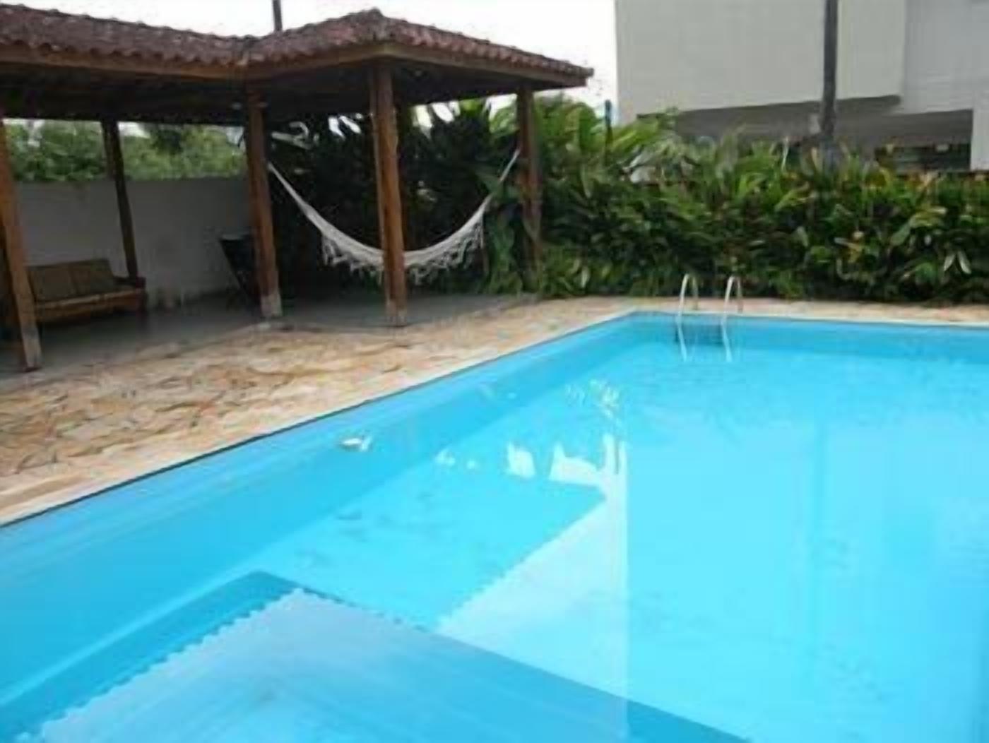 Une piscine rectangulaire à l’eau d’un bleu cristallin, entourée d’une terrasse en pierre et agrémentée d’une pergola en bois avec un hamac.