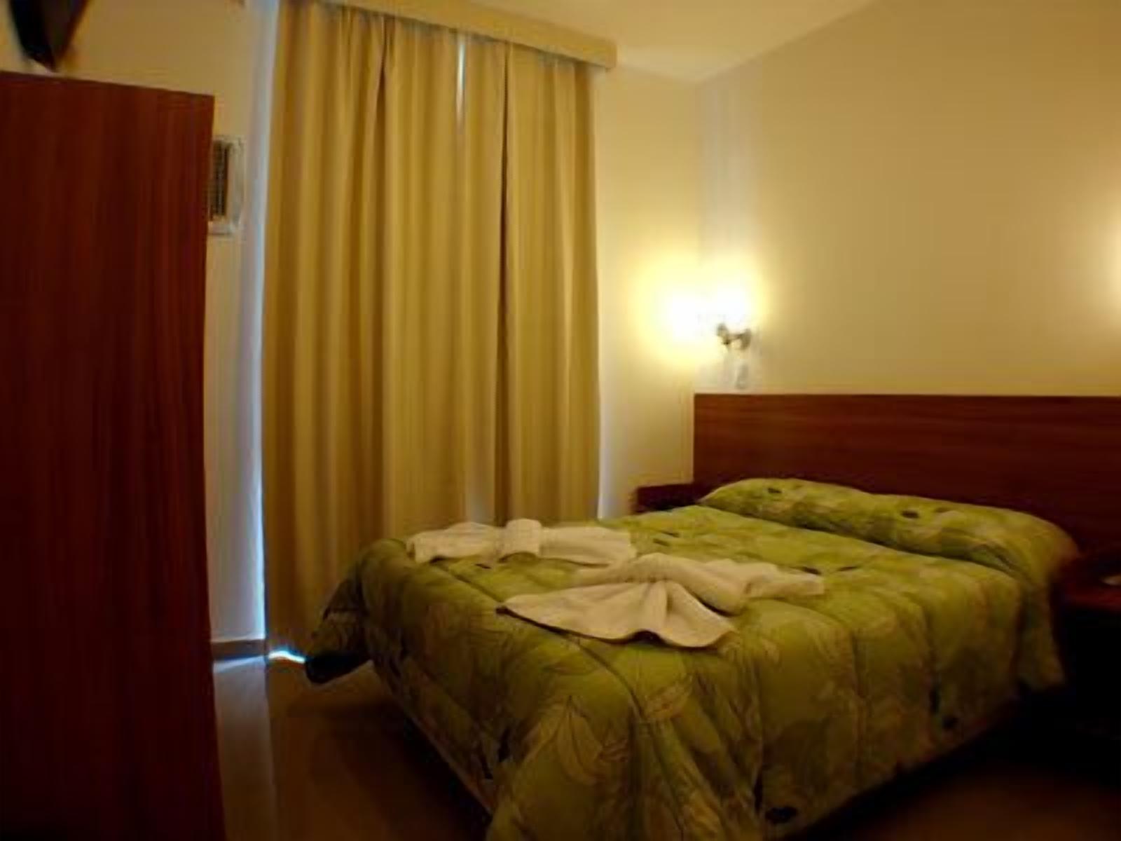 A hotel room with a bed, curtains, and a nightstand.