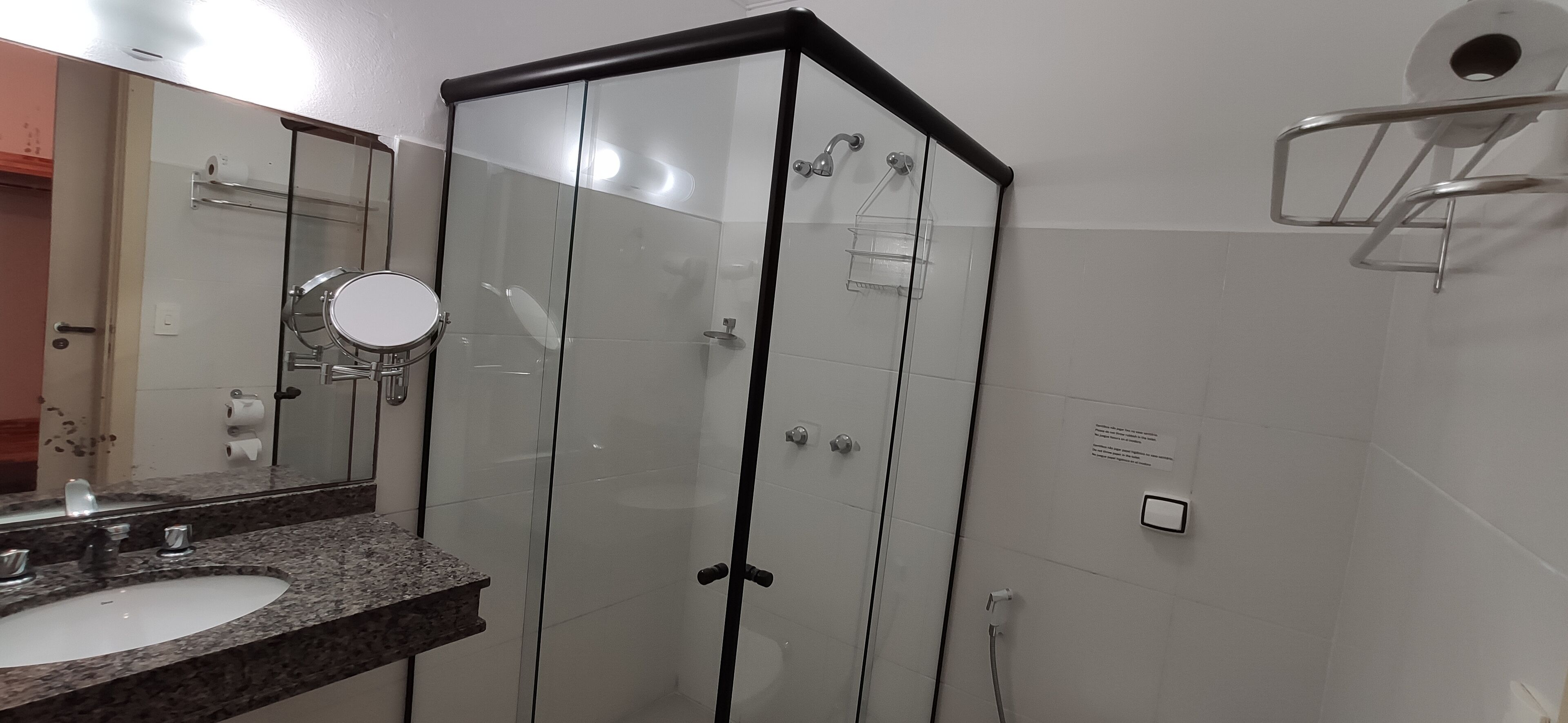 Een moderne badkamer met een douchecabine van glas, een wastafel met granieten blad en een spiegel.