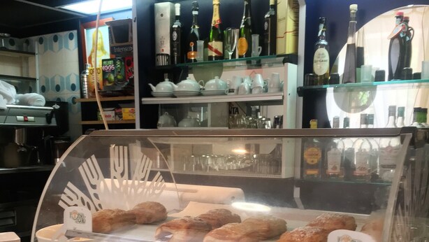 Een bakkerij etalage met diverse gebakjes en een assortiment gebottelde drankjes op de achtergrond.