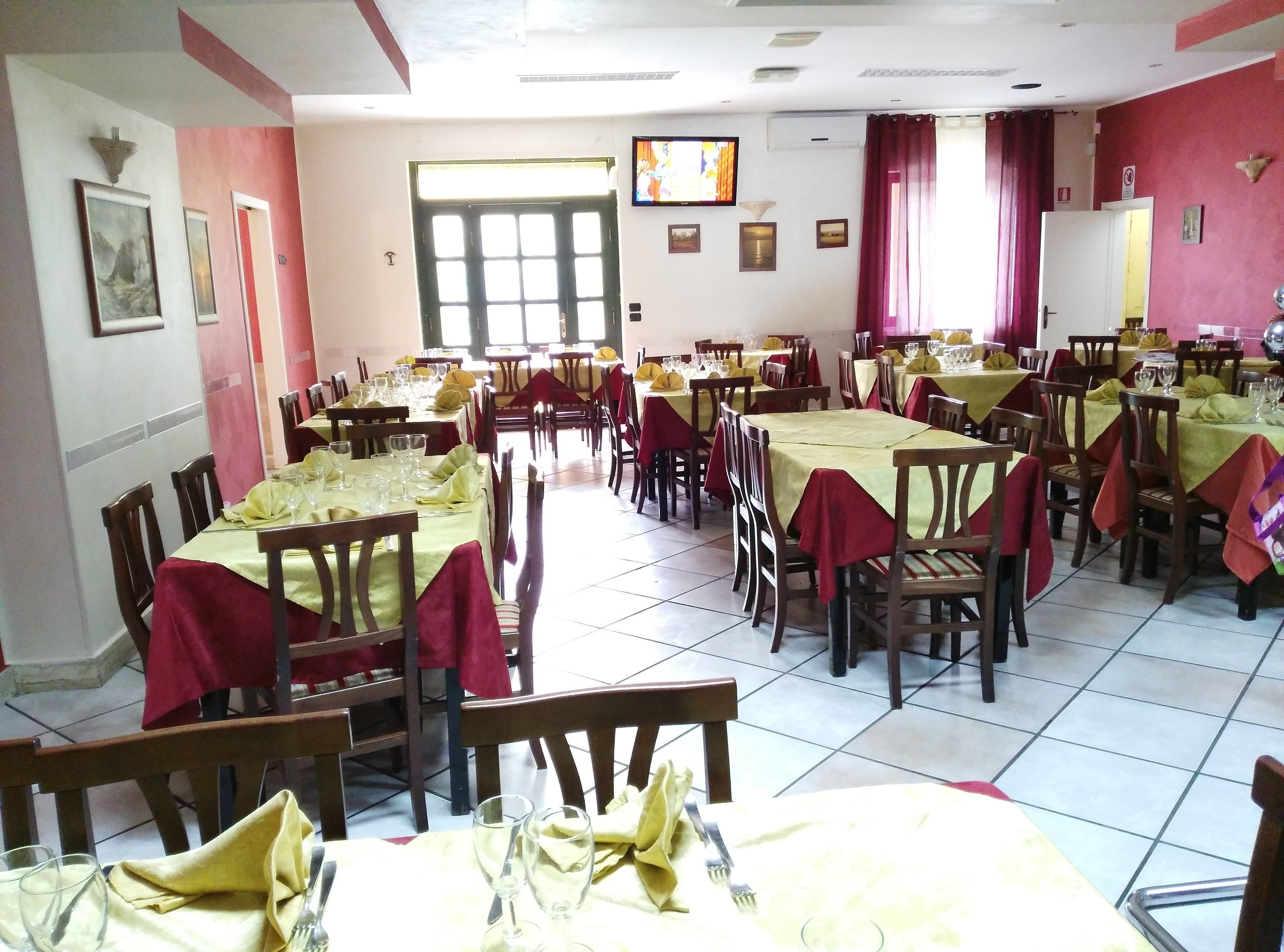 A dining area with multiple tables set for service, chairs, and a television on the wall.