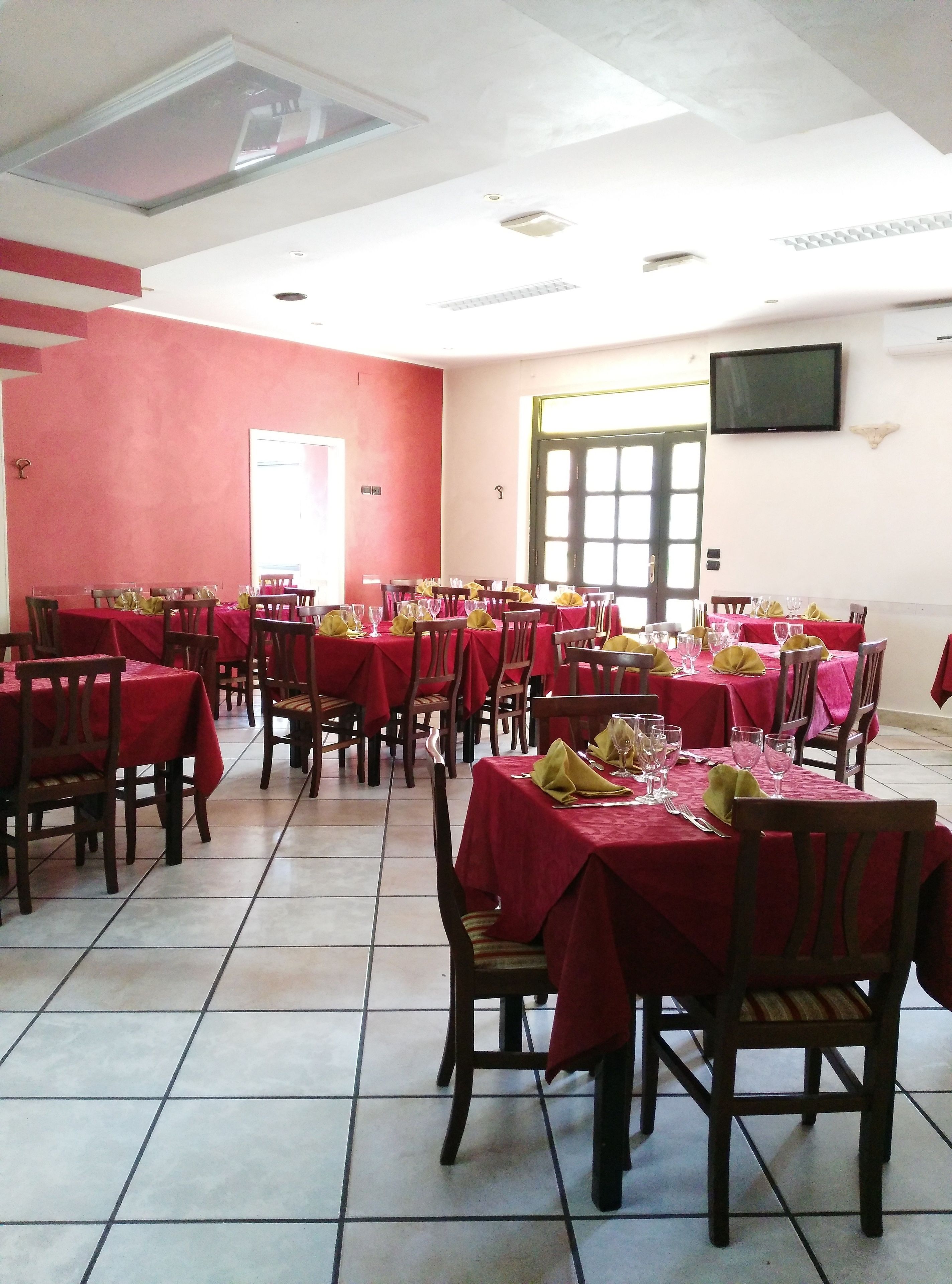 A dining area with multiple tables covered in red tablecloths, arranged in rows.