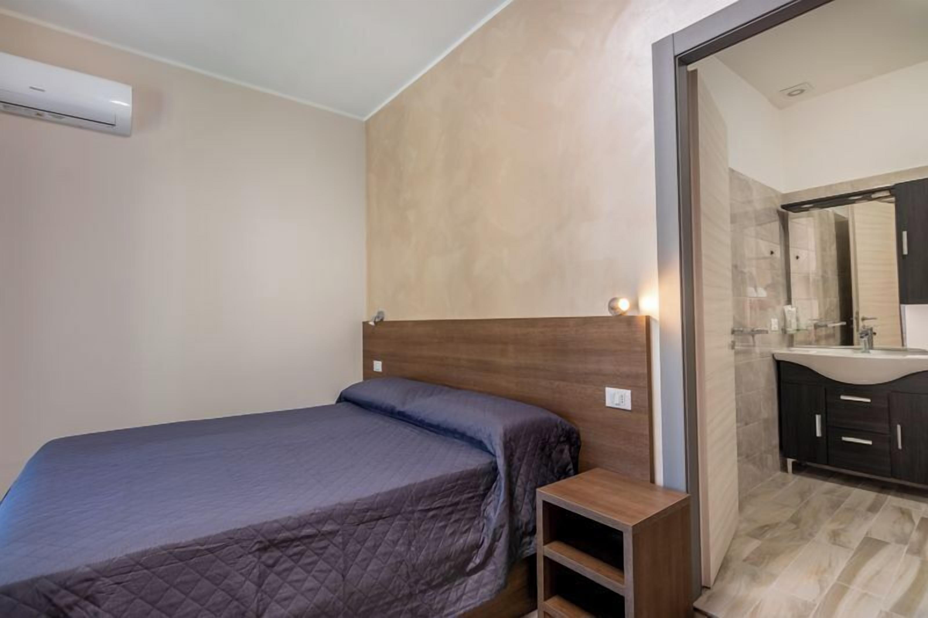 Un dormitorio con cama, mesita de noche y baño con espejo y lavabo.