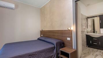 A bedroom with a bed, a nightstand, and a bathroom with a mirror and sink.