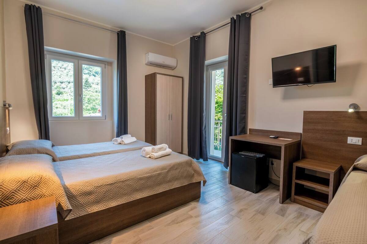 A hotel room with two beds, a desk, a TV, and an air conditioning unit.