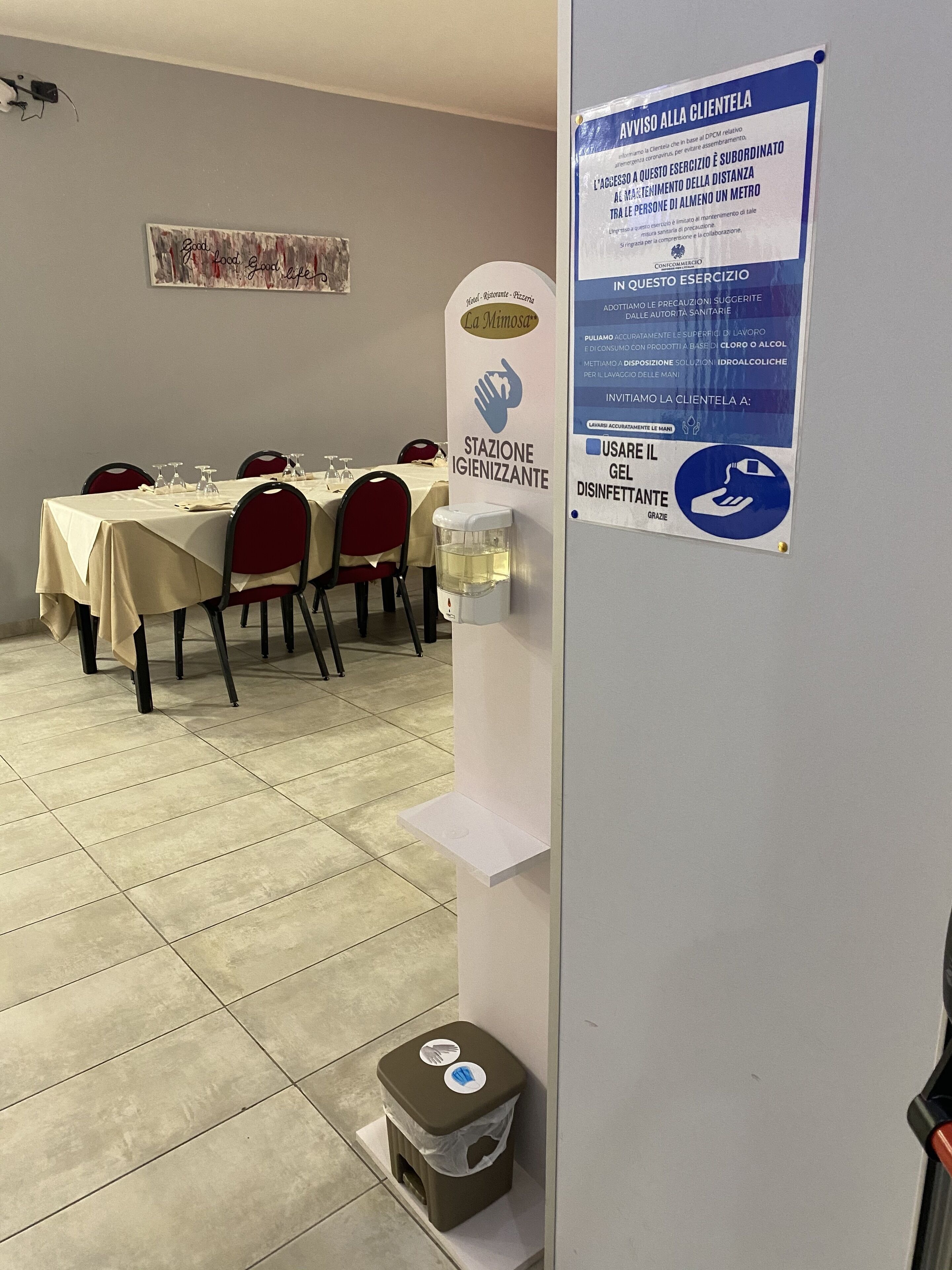 Un espace repas avec des tables dressées pour le service, un distributeur de solution hydroalcoolique et un panneau affichant les consignes d’hygiène et de sécurité.