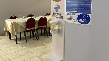 Un espace repas avec des tables dressées pour le service, un distributeur de solution hydroalcoolique et un panneau affichant les consignes d’hygiène et de sécurité.