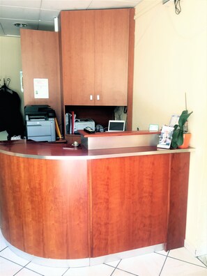 A reception desk with a wooden finish, a printer, a computer, and a small plant.