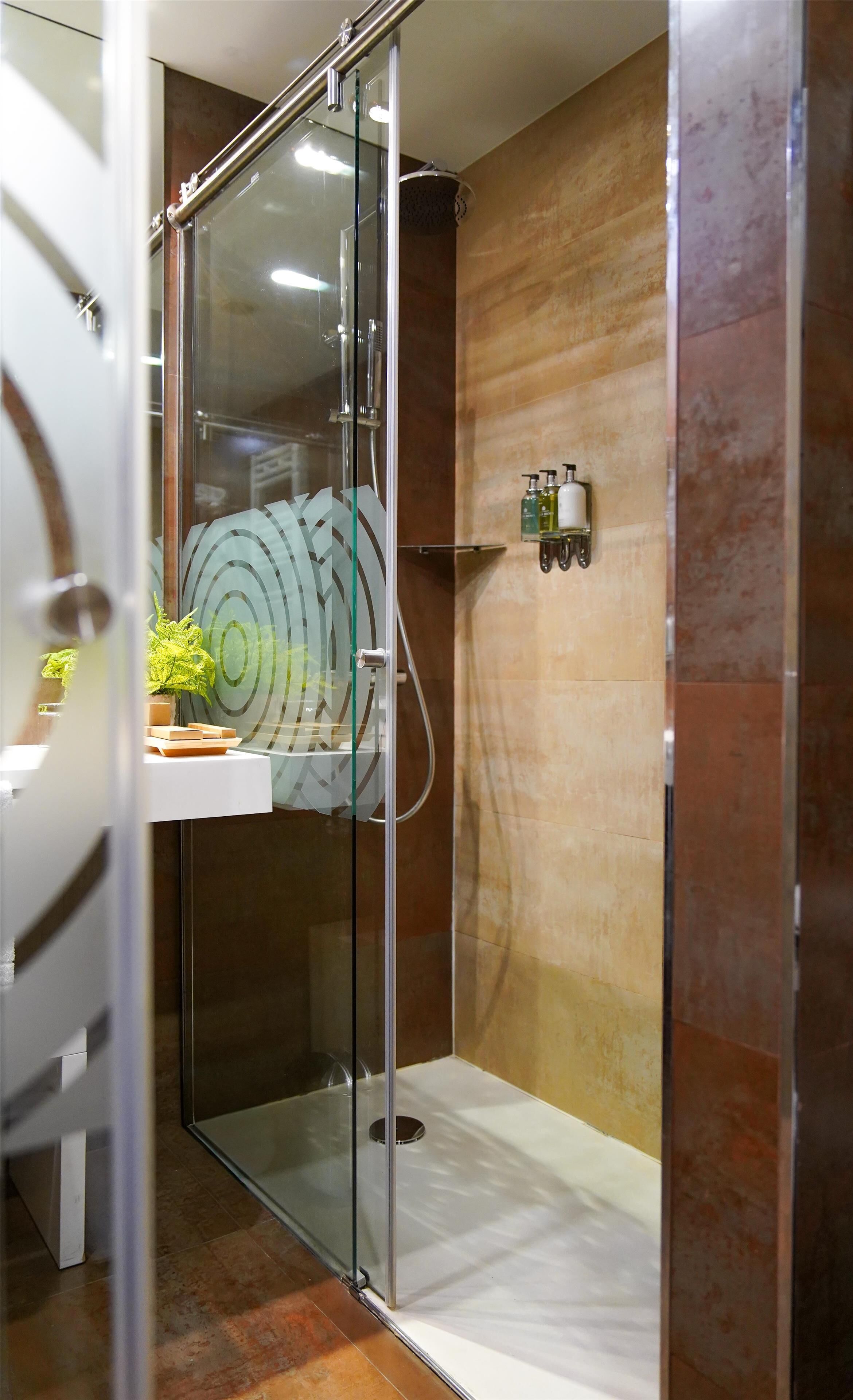A modern bathroom with a glass-enclosed shower, a white sink with a soap dispenser, and a potted plant on the counter.