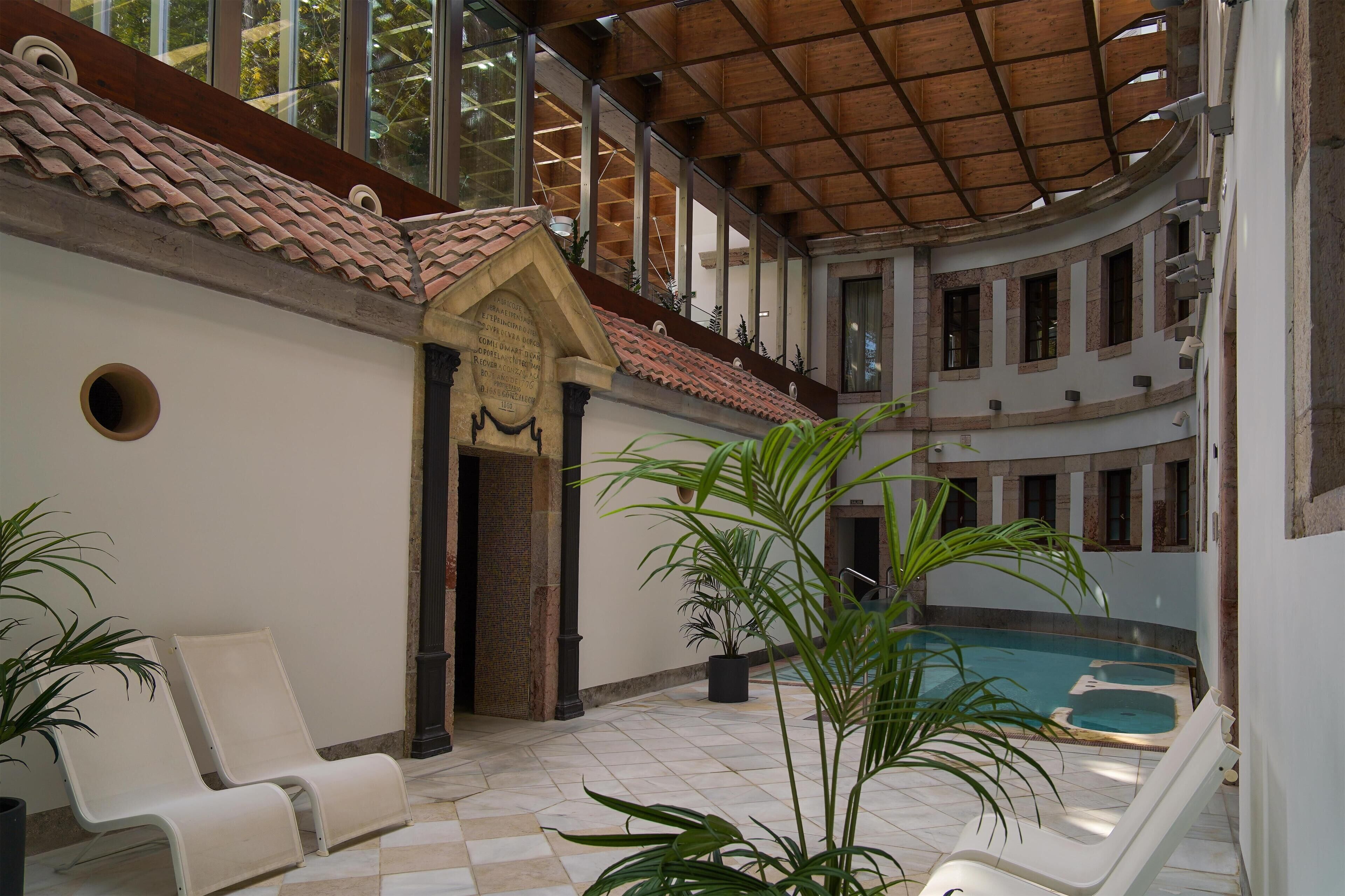 Un amplio espacio interior con piscina, sillas de descanso y plantas en macetas.