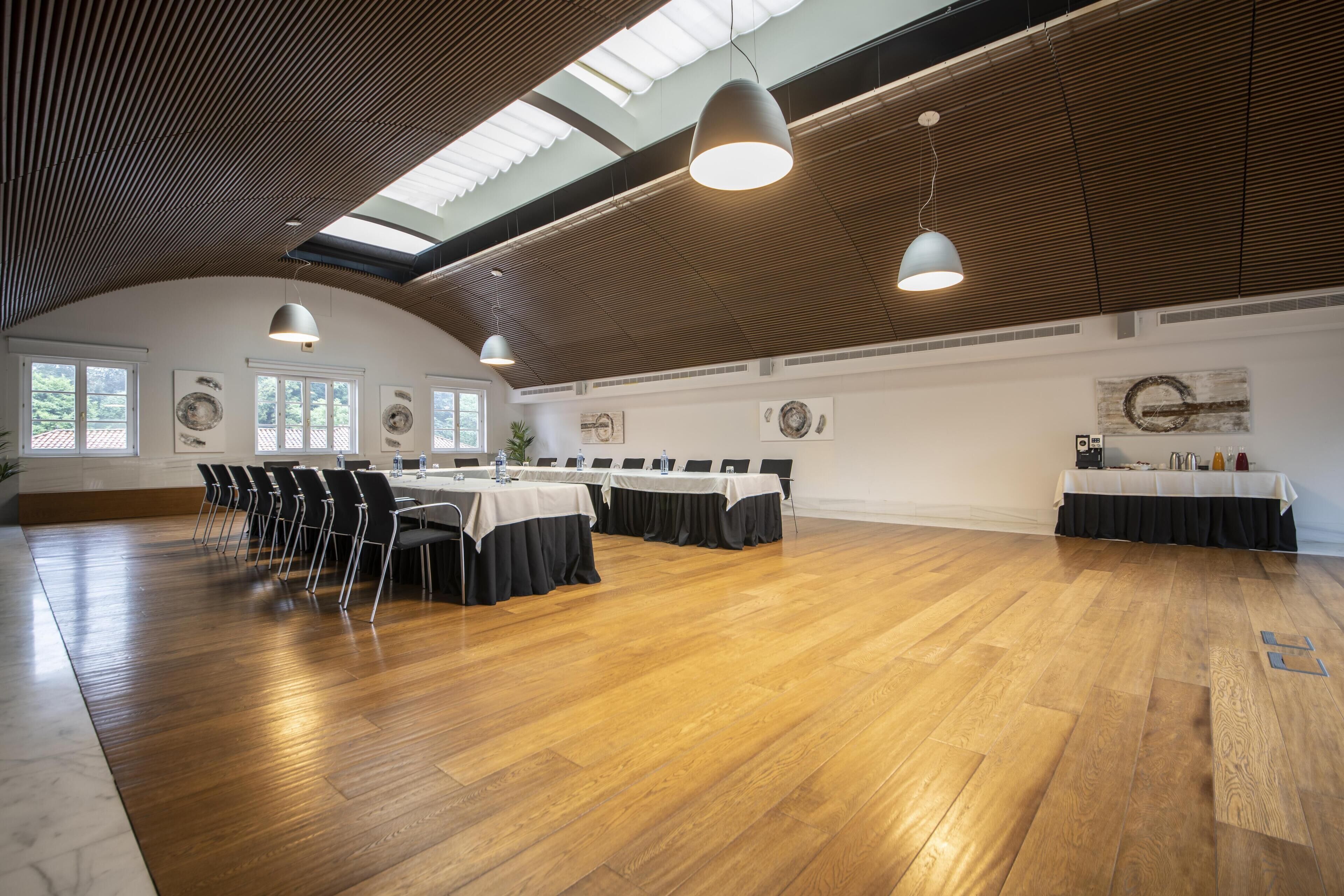 Une salle de conférence spacieuse, dotée de parquets en bois, de longues tables et de chaises noires.