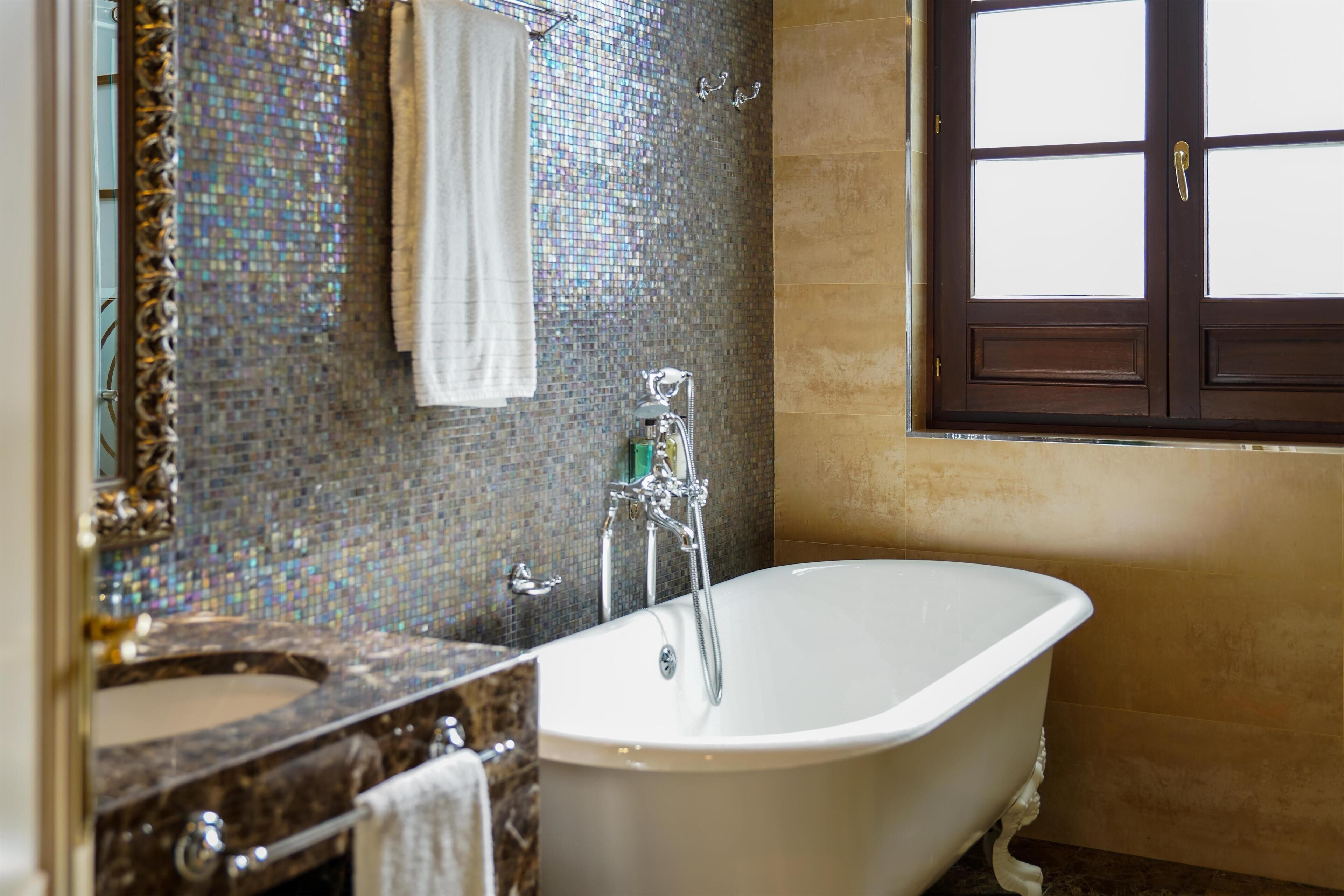 A bathroom with a freestanding bathtub, a sink with a marble countertop, and a mosaic-tiled wall.