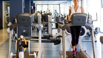Ein Fitnessstudio mit Laufbändern, Trainingsgeräten und einer Person, die ein Laufband benutzt.