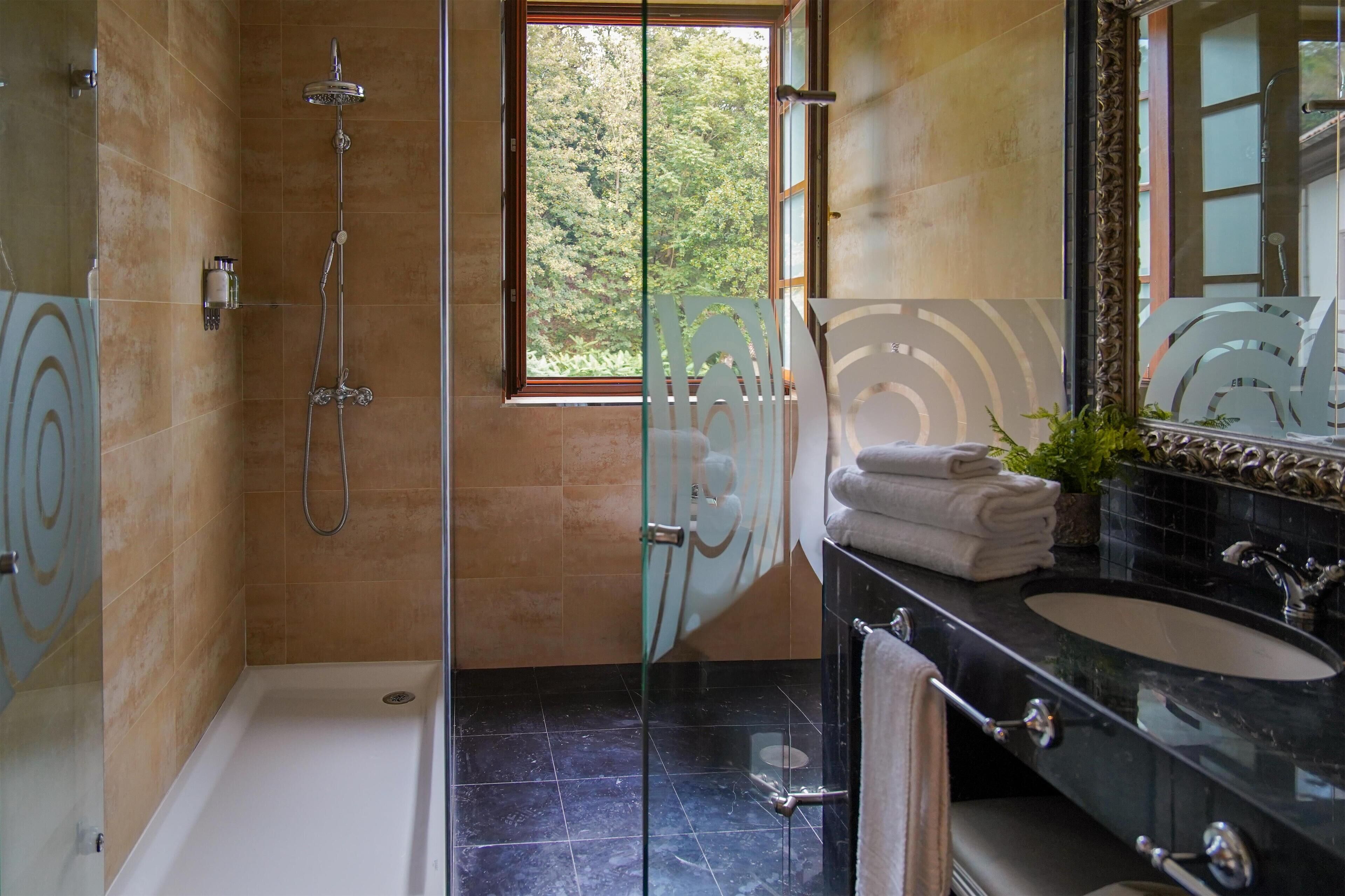 A bathroom with a glass-enclosed shower, a bathtub, a vanity with a black countertop, and a large mirror.