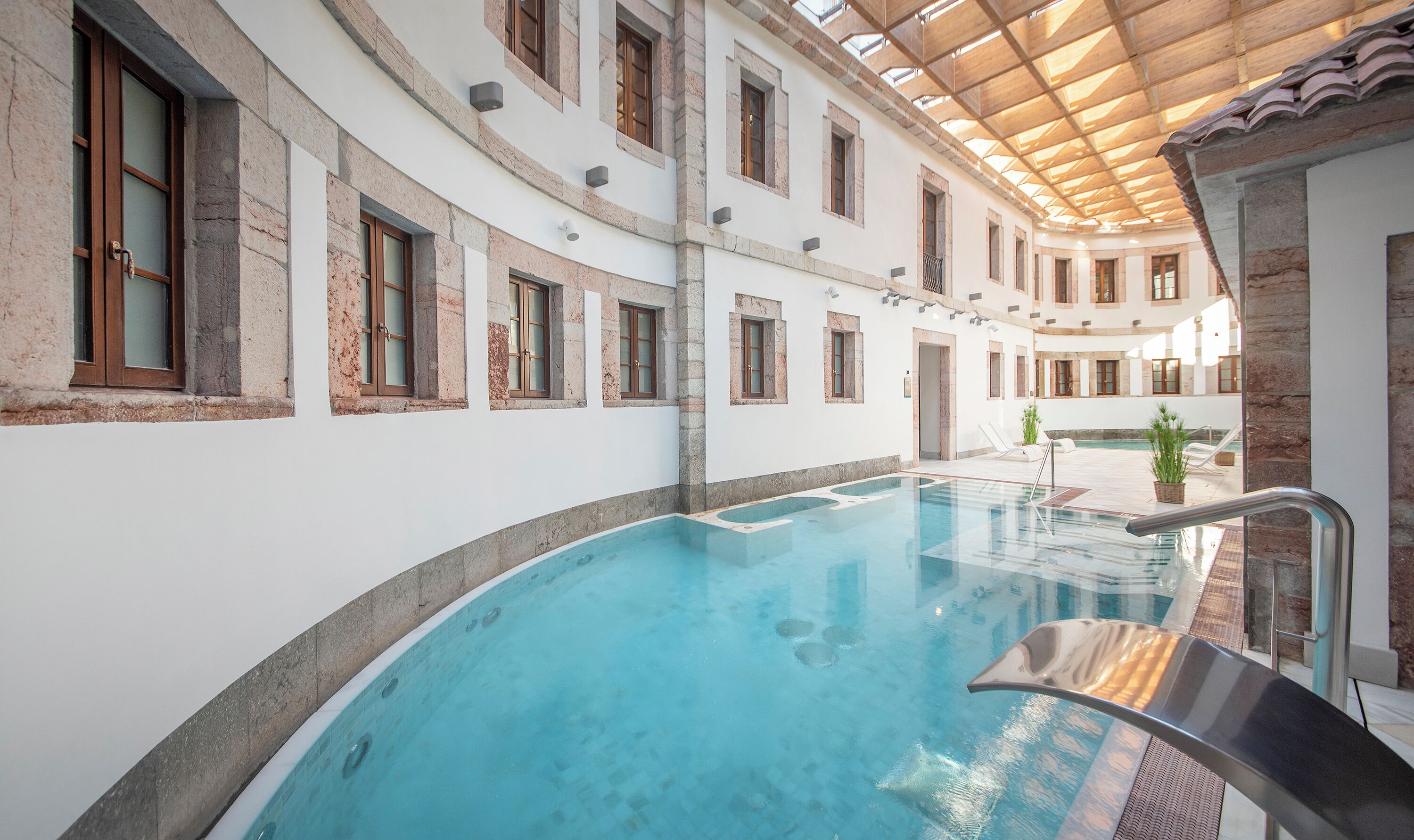 Una piscina interior con agua cristalina, rodeada de muros de piedra y vigas de madera.