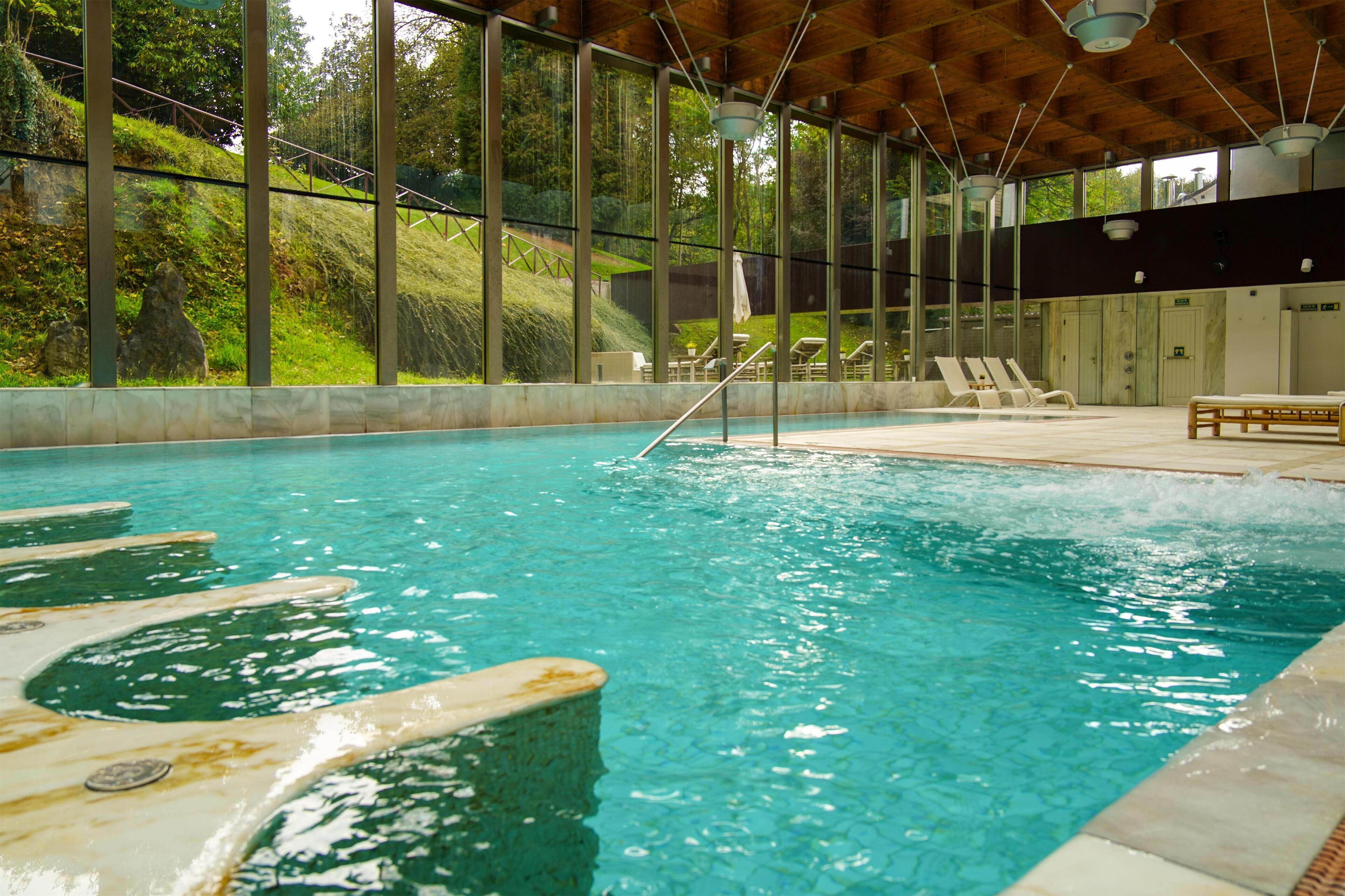 An indoor swimming pool with clear water, surrounded by lounge chairs and a wooden ceiling.