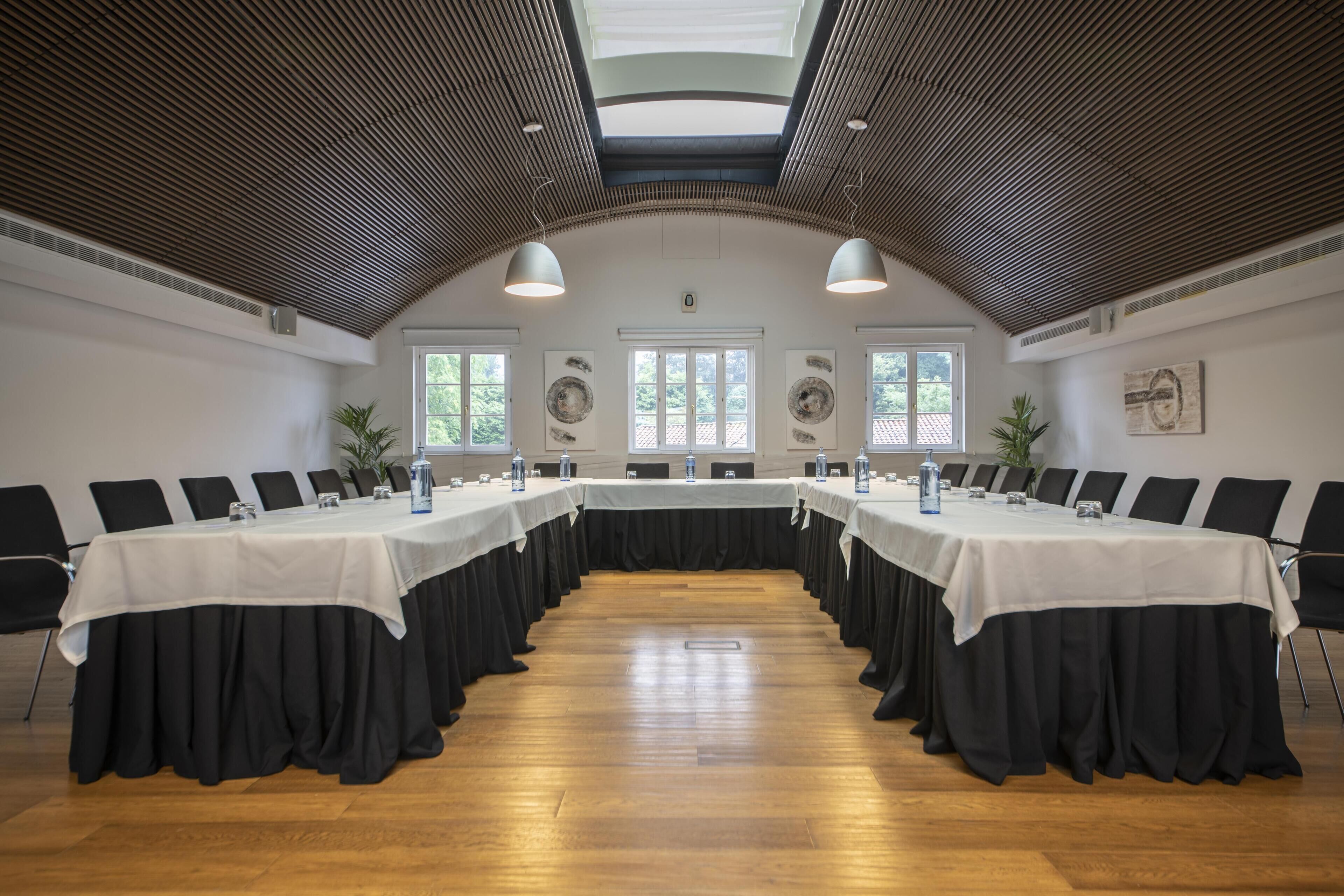 Ein Konferenzraum mit einem langen Tisch, schwarzen Stühlen und weißen Tischdecken.