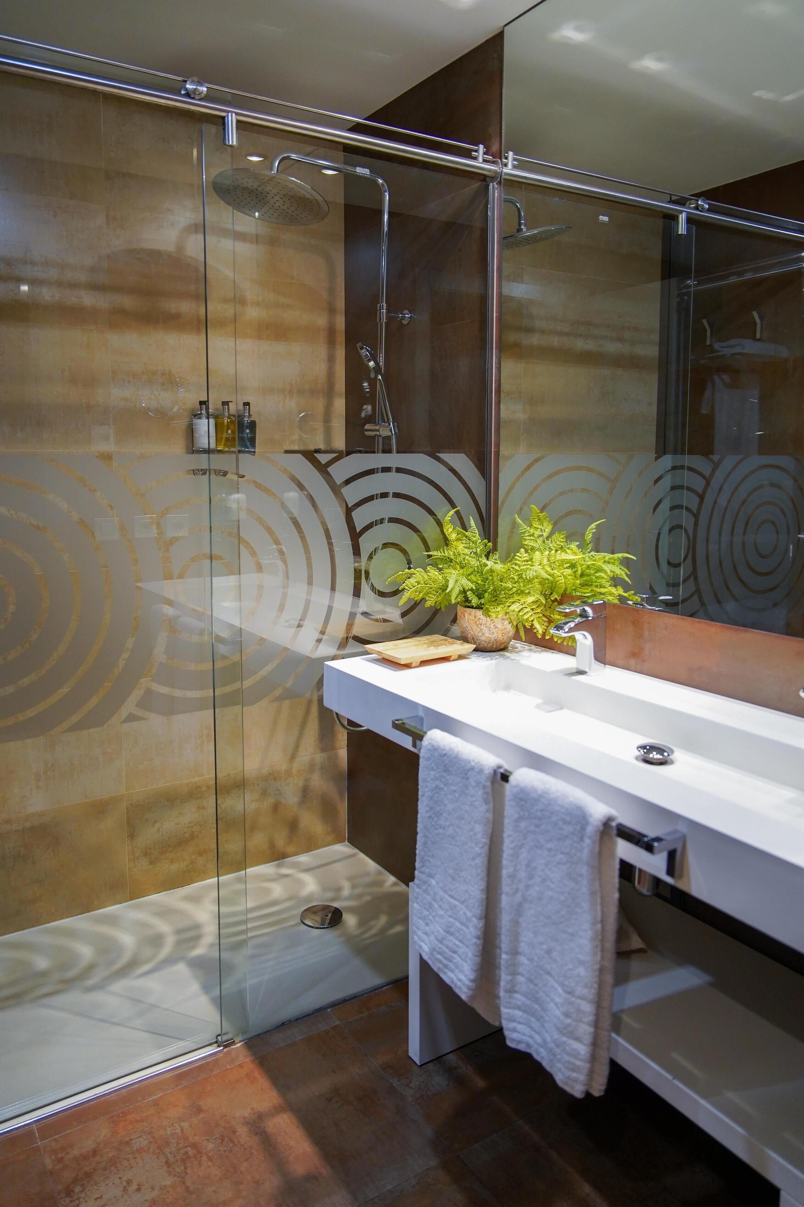 Een moderne badkamer met een douchecabine van glas, een witte wastafel en een spiegel met een rond ontwerp.