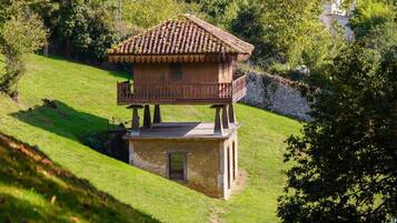 A wooden house with a balcony on a grassy hill, surrounded by trees and hills.