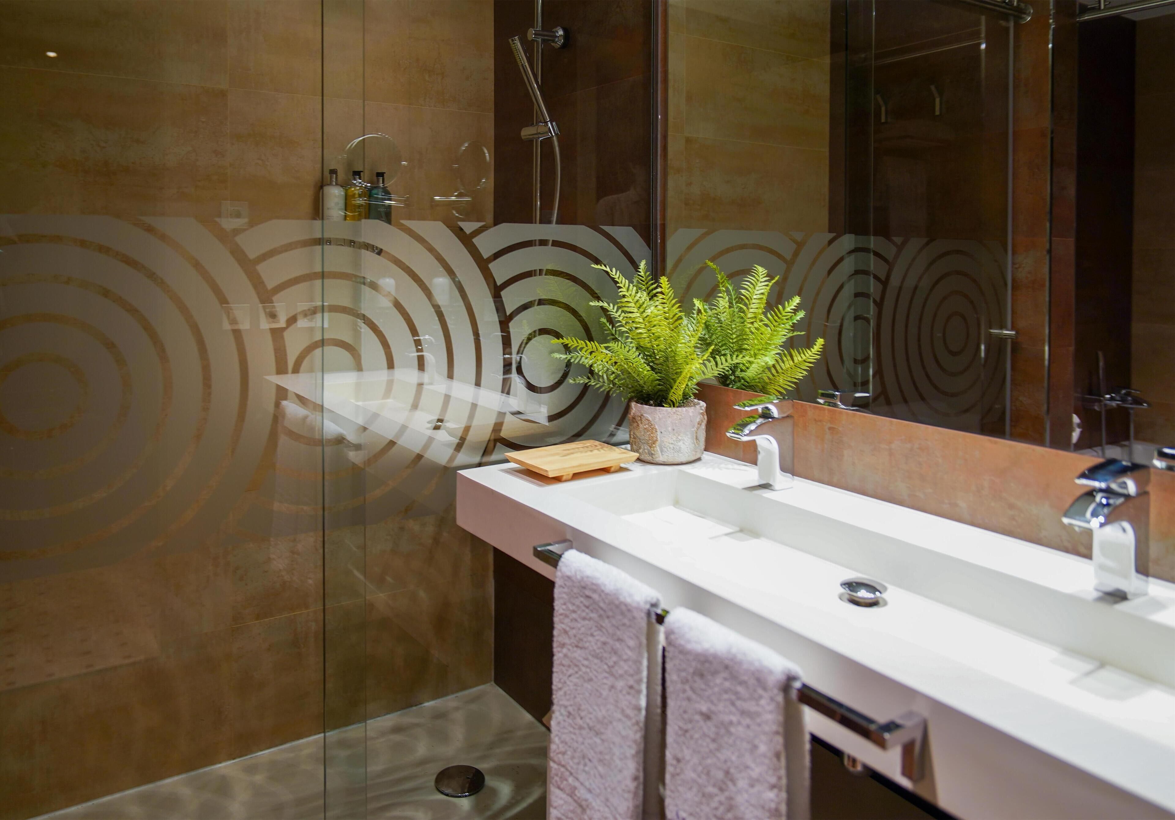 A modern bathroom with a glass shower enclosure, a white sink, and a potted plant.