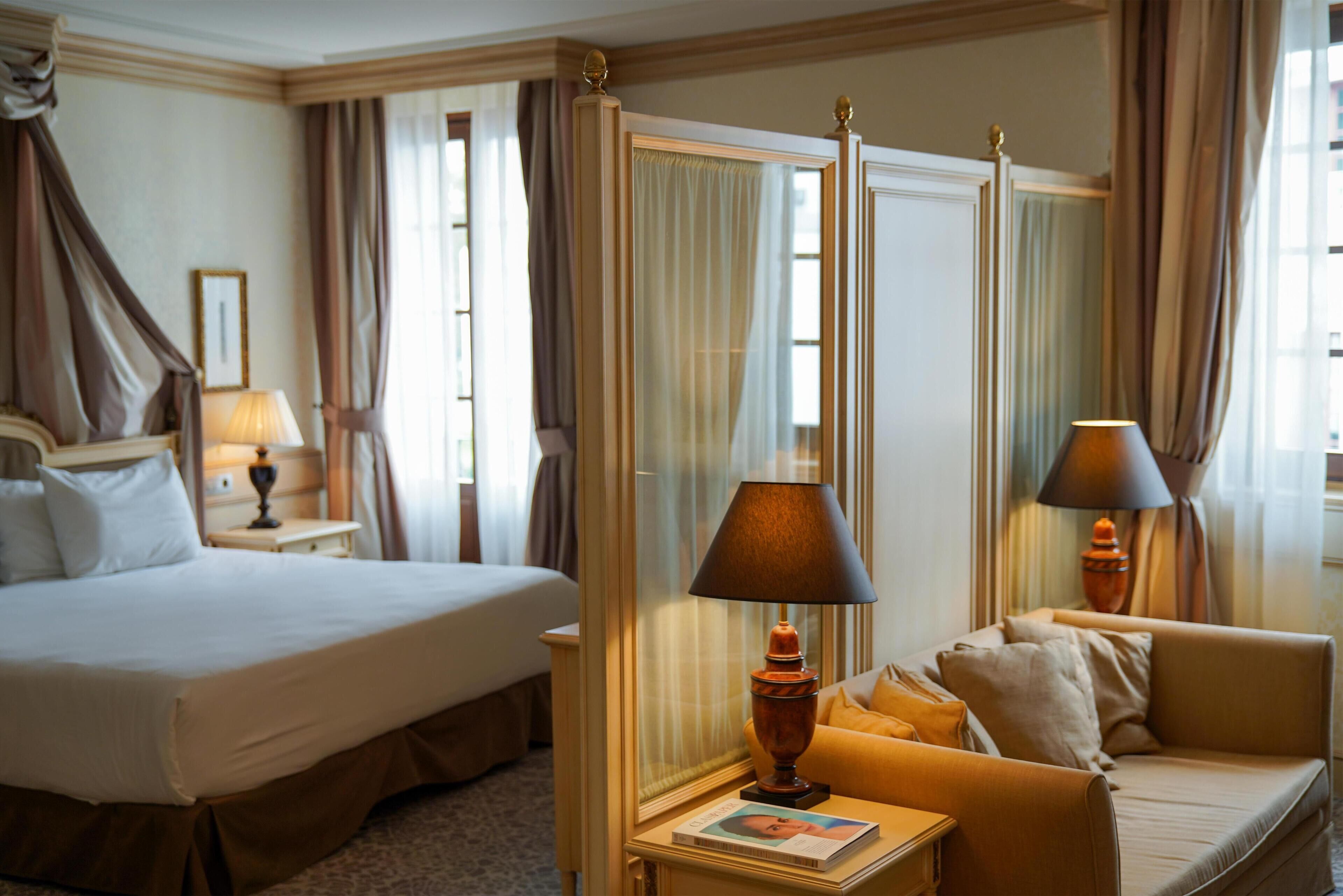 A hotel room with a large bed, a sofa, a nightstand with a lamp, and a mirror.