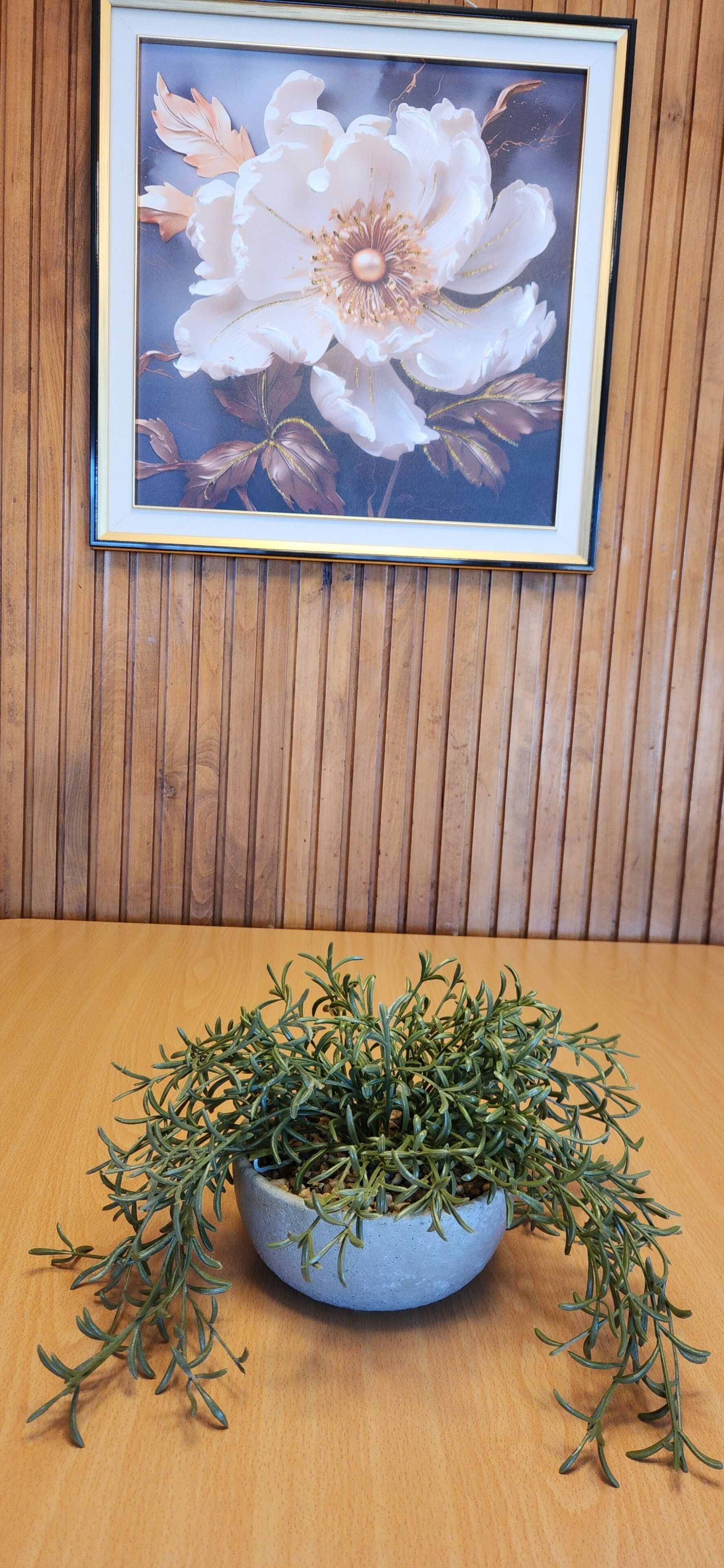 Una obra de arte floral enmarco sobre una pared de madera, una planta en maceta con follaje verde sobre una mesa de madera.