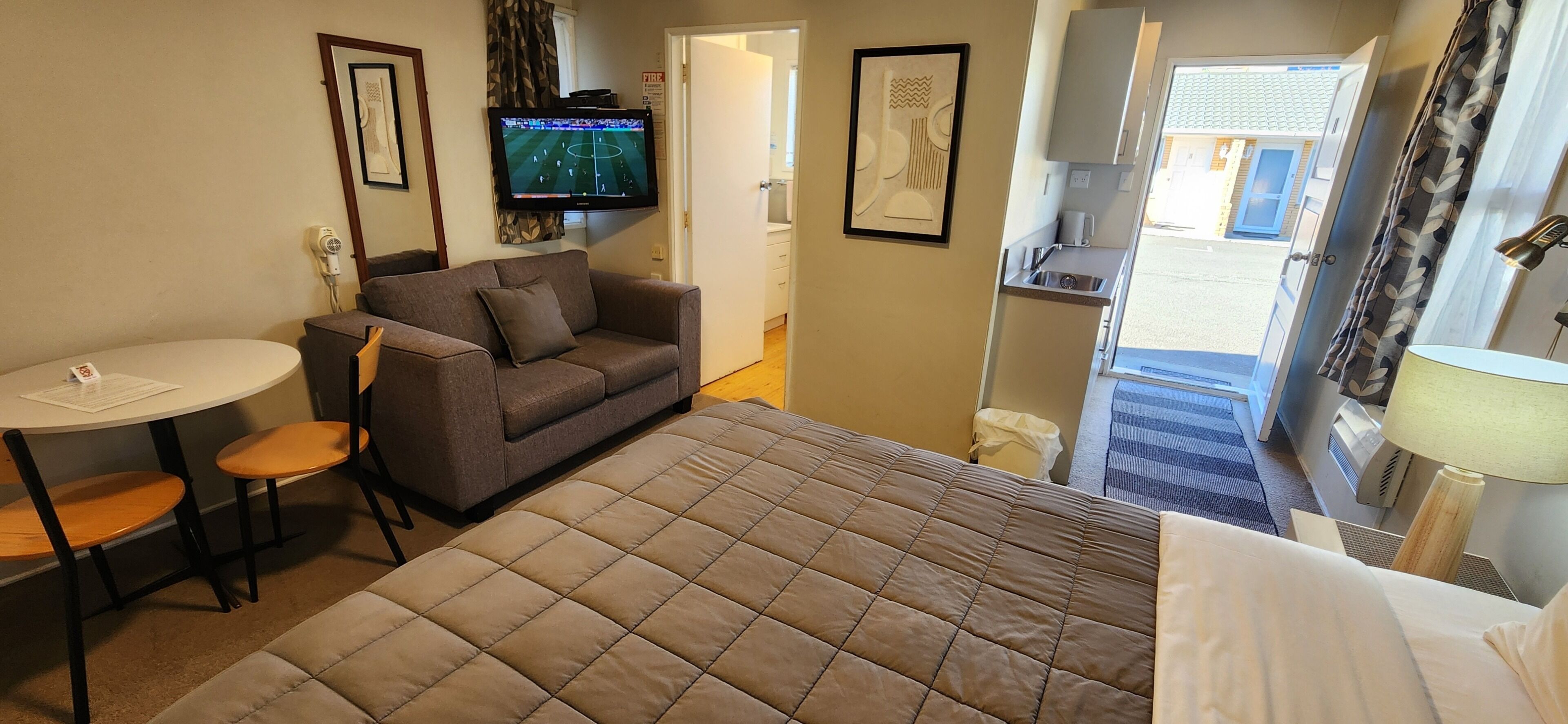 A hotel room with a bed, a sofa, a small table, a TV, and a kitchen area.