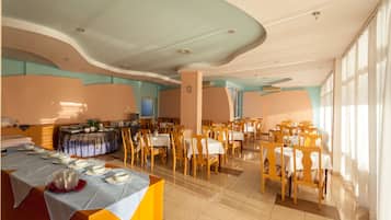 Un vaste espace dédié à la salle à manger, avec plusieurs tables et chaises, un buffet et une grande fenêtre laissant entrer la lumière naturelle.