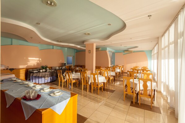 A spacious dining area with multiple tables and chairs, a buffet setup, and a large window providing natural light.