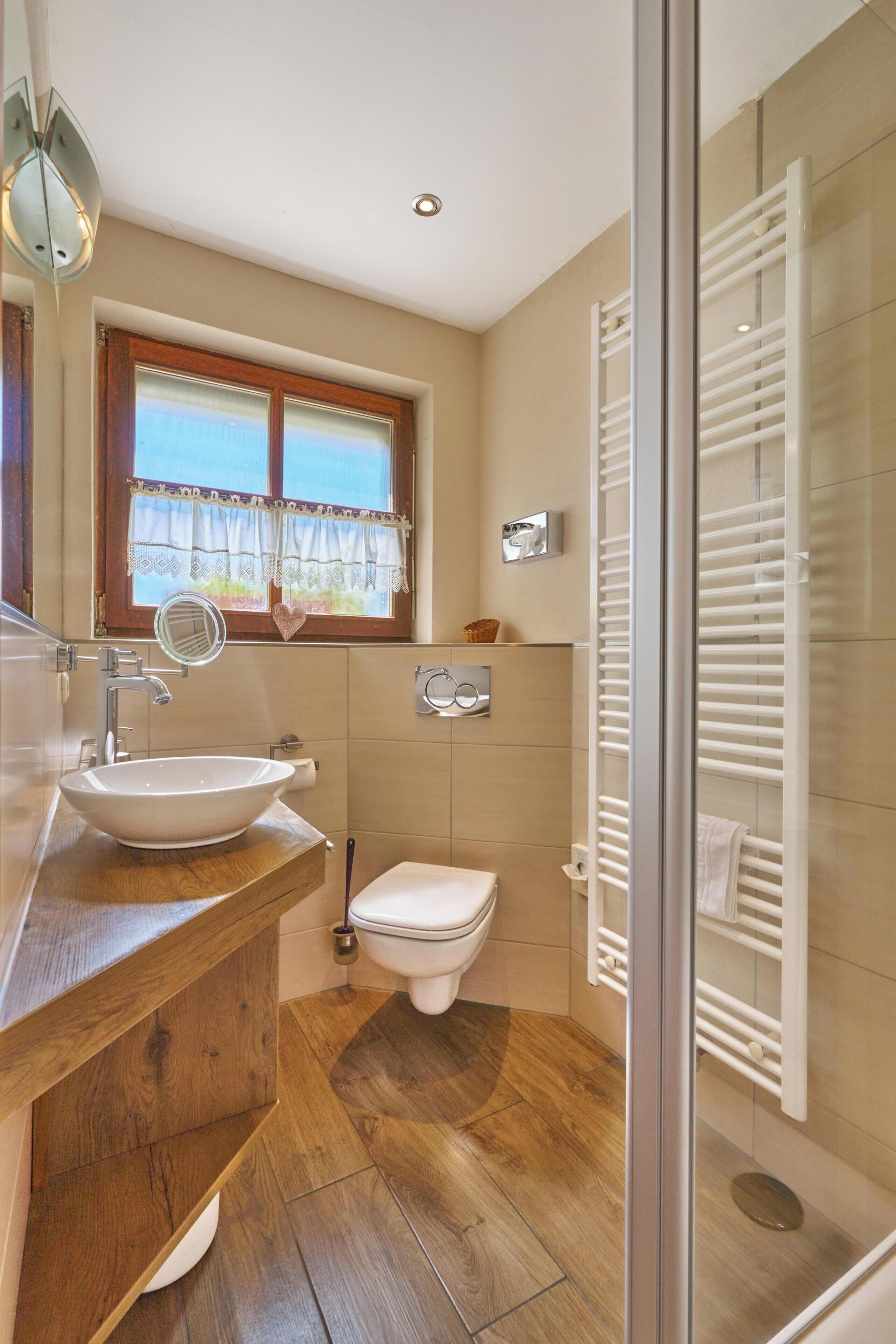 A bathroom with a wooden vanity, a vessel sink, a toilet, a window with a view, and a glass shower enclosure.