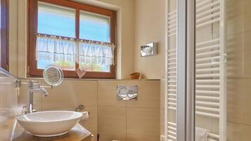 A bathroom with a wooden vanity, a vessel sink, a toilet, a window with a view, and a glass shower enclosure.