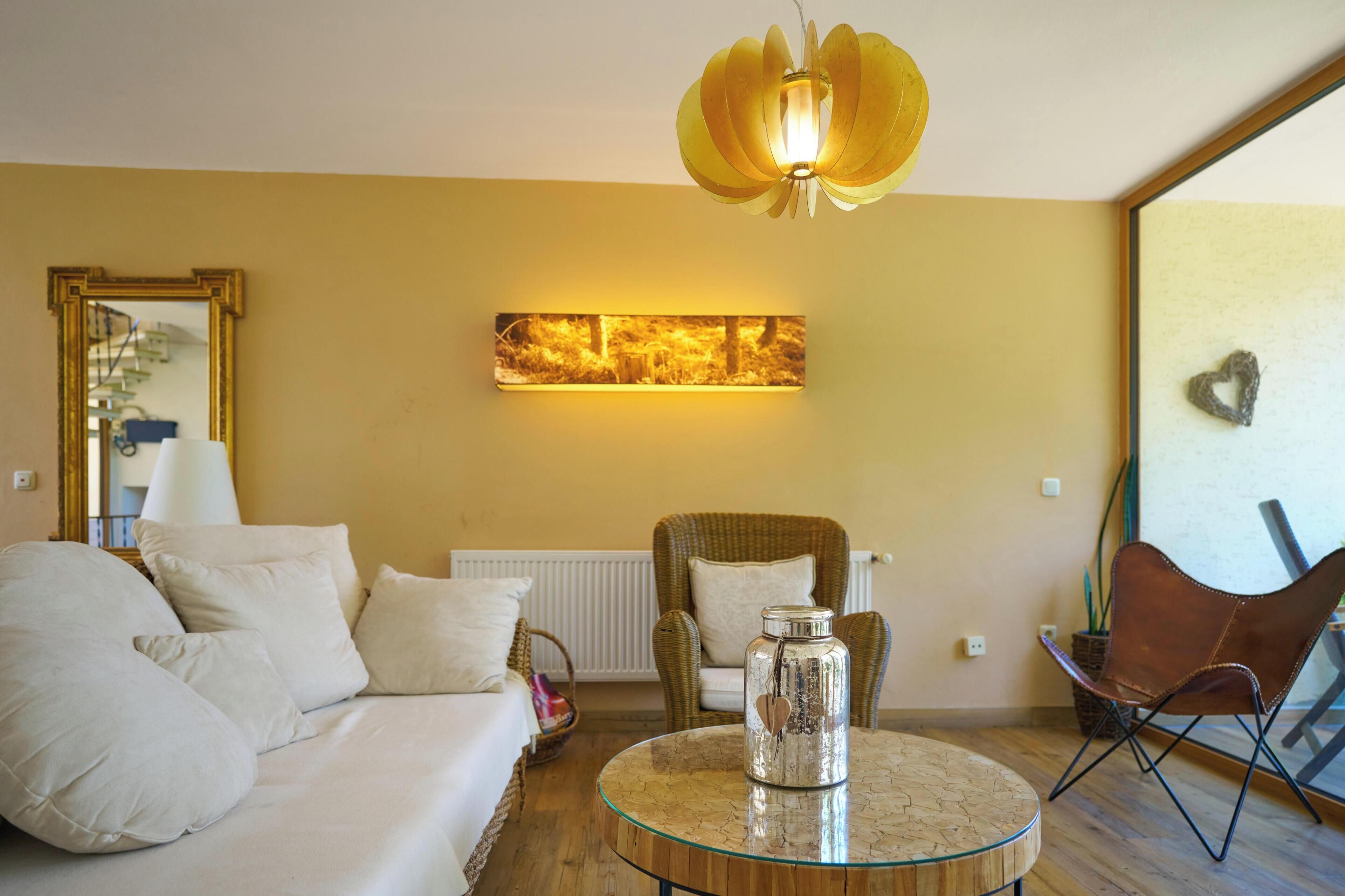 A living room with a sofa, a chair, a glass coffee table, a pendant light, a radiator, and a wall-mounted picture.