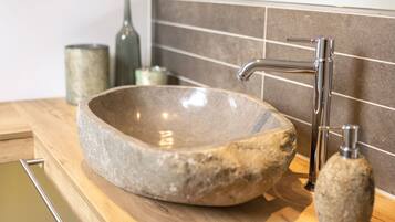 Un lavabo in pietra con un rubinetto moderno, un piano di lavoro in legno e uno schienale rivestito di piastrelle.