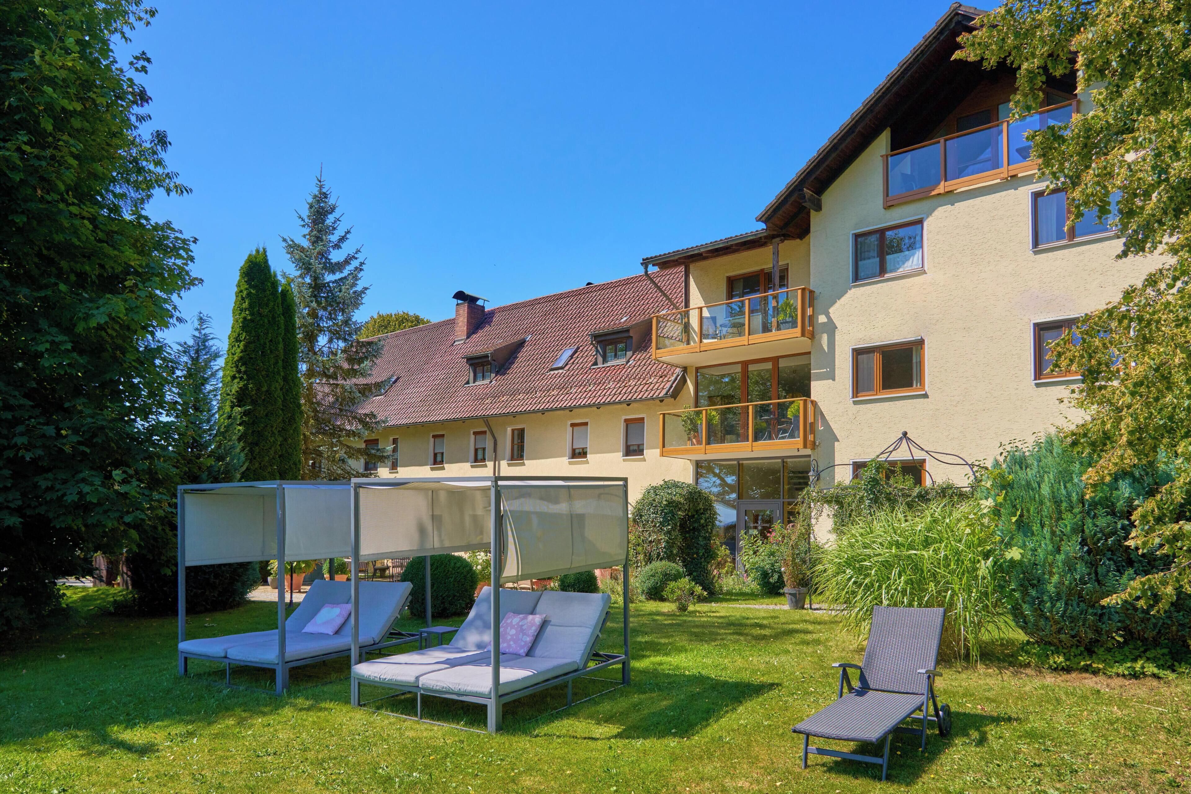 Ein zweistöckiges Gebäude mit Balkon, ein Garten mit Liegestühlen und einem strahlend blauen Himmel.
