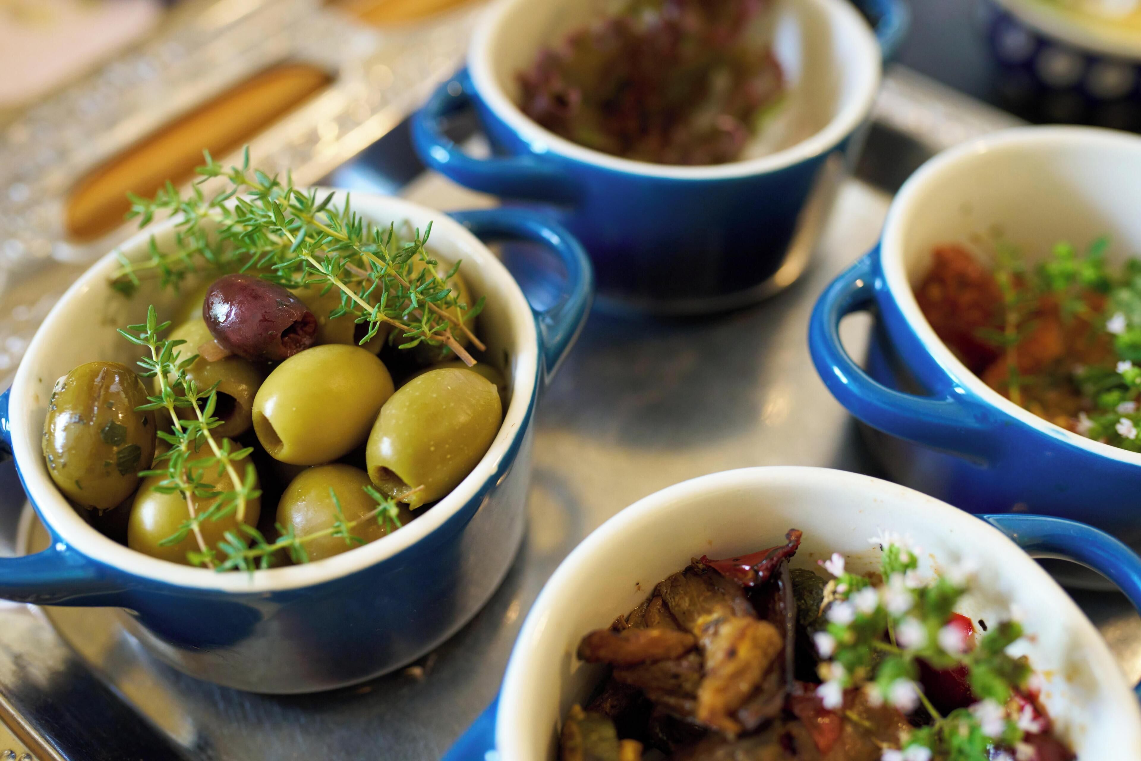 Una bandeja con diversos platos, incluyendo aceitunas y hierbas, y un bol con carne y verduras.