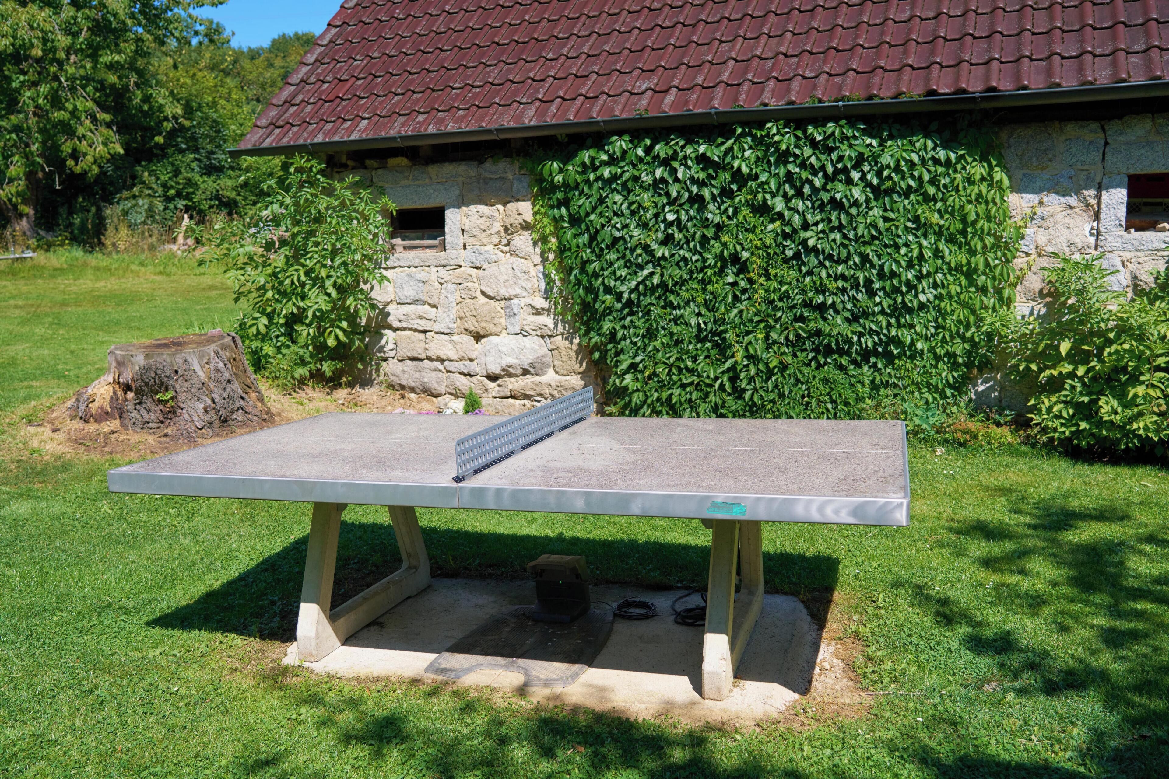 A stone building with a red-tiled roof, a concrete bench in front, and a hedge behind.