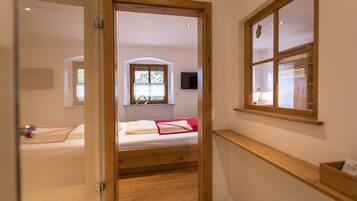Ein schmaler Flur führt zu einem Schlafzimmer mit einem hölzernen Bett, einem Fenster und einem Fernseher an der Wand.
