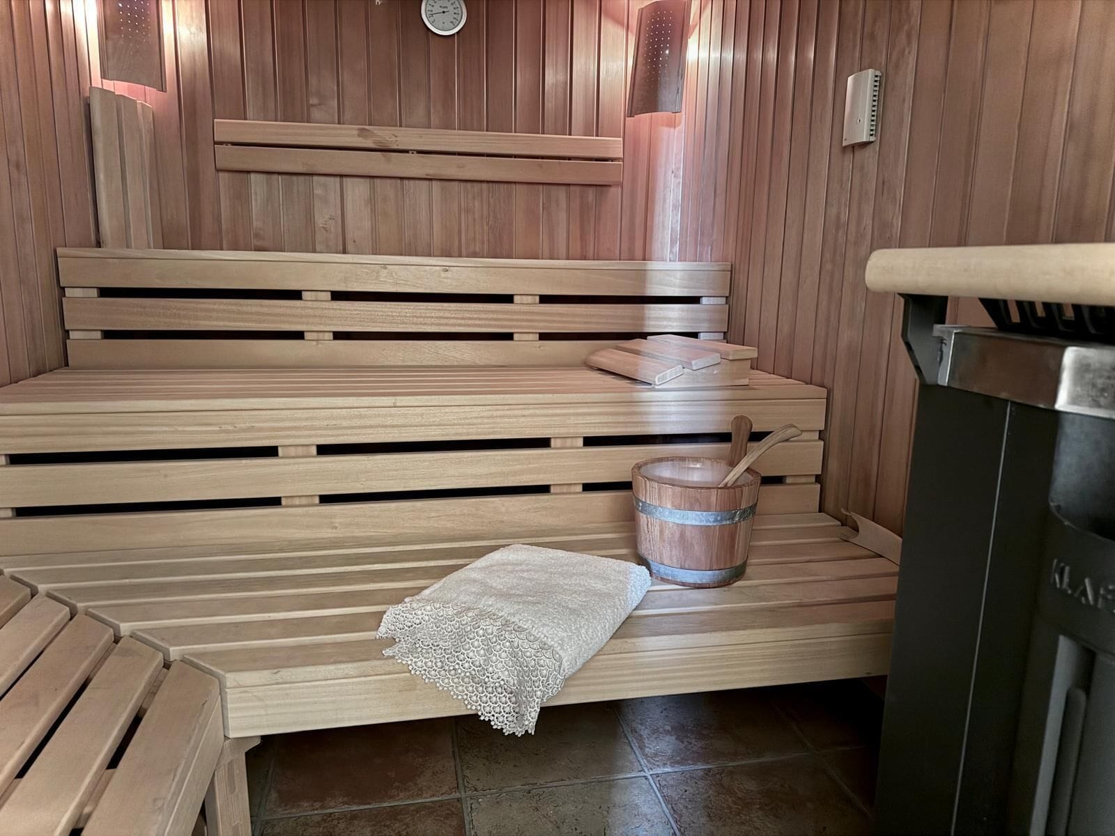 Una sauna de madera con bancos, un balde de madera y una toalla.