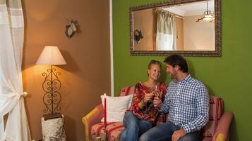 Een paar personen zitten op een rood-wit gestreepte bank, met een salontafel met houtblokken, een lamp, een spiegel aan de muur en een decoratieve dierenkop.