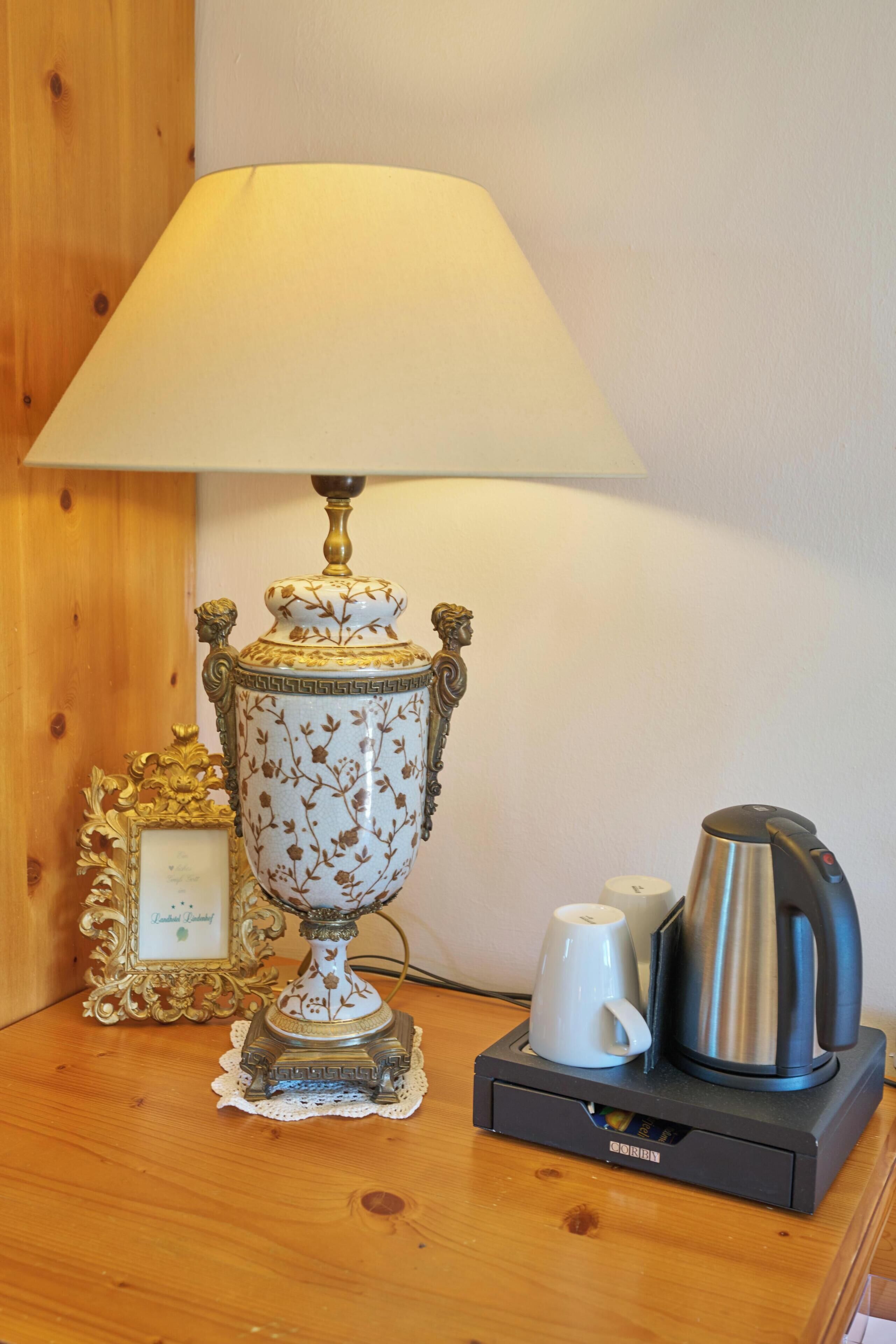 A table with a decorative lamp, a framed picture, a white mug, and a coffee maker.