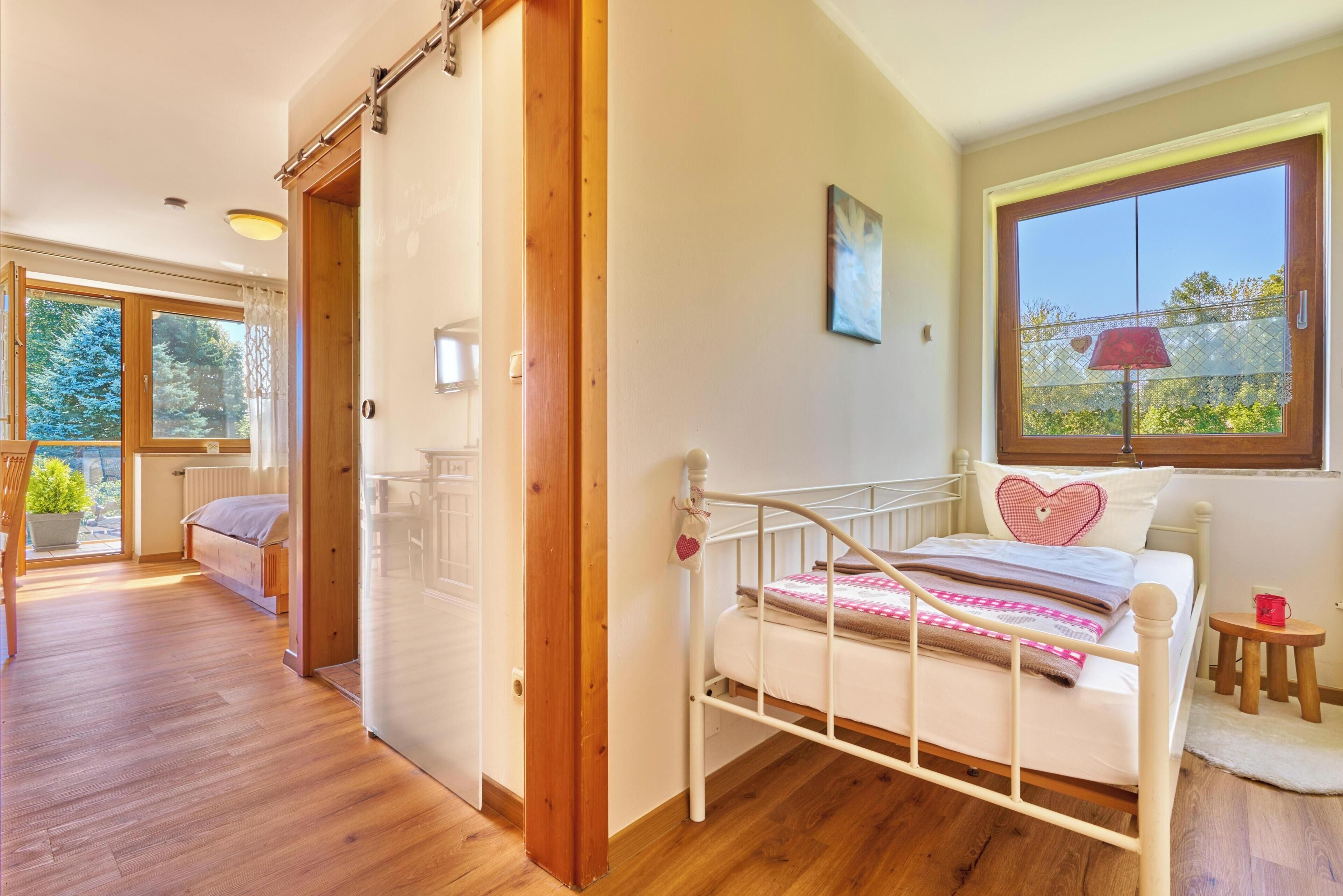Une chambre à coucher avec un lit, une fenêtre donnant sur un beau paysage, une porte et un petit tabouret.
