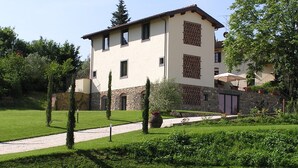 Un edificio de dos pisos con base de piedra y un nivel superior color beige, rodeado de un jardín bien cuidado con un sendero de grava.
